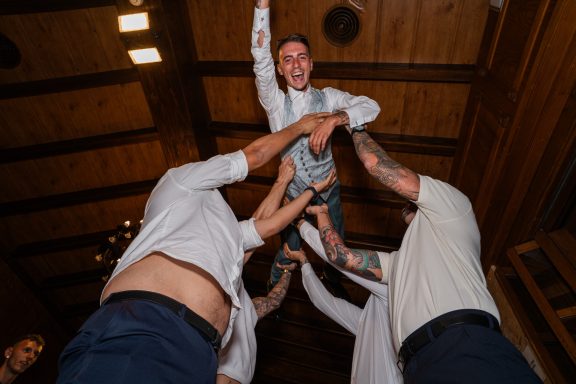 Un grupo de personas levanta a un joven durante una celebración en un lugar con madera.